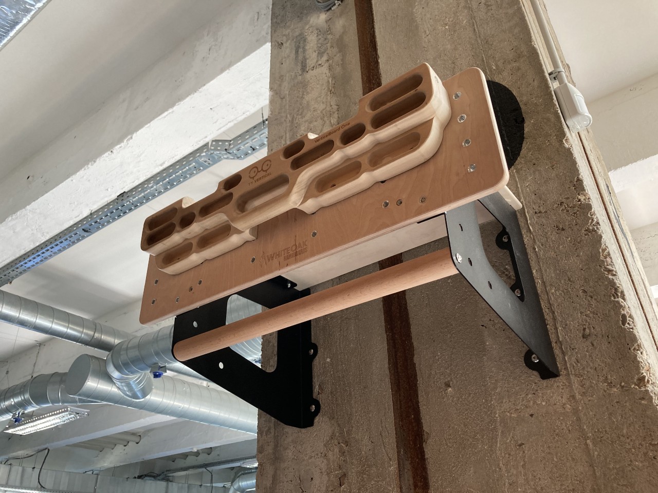 Poutre d’escalade en bois fixée sur un mur en béton dans un espace intérieur industriel.
