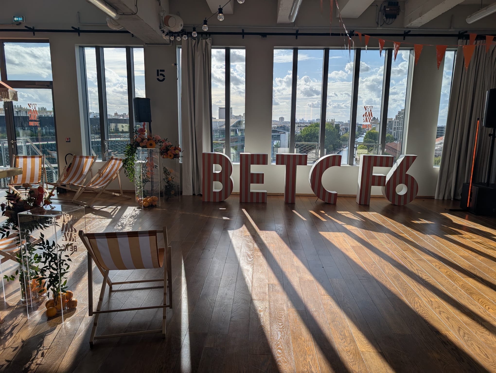 Salle lumineuse décorée pour un événement BETC F6, grandes lettres rouges posées devant des baies vitrées avec vue sur la ville.