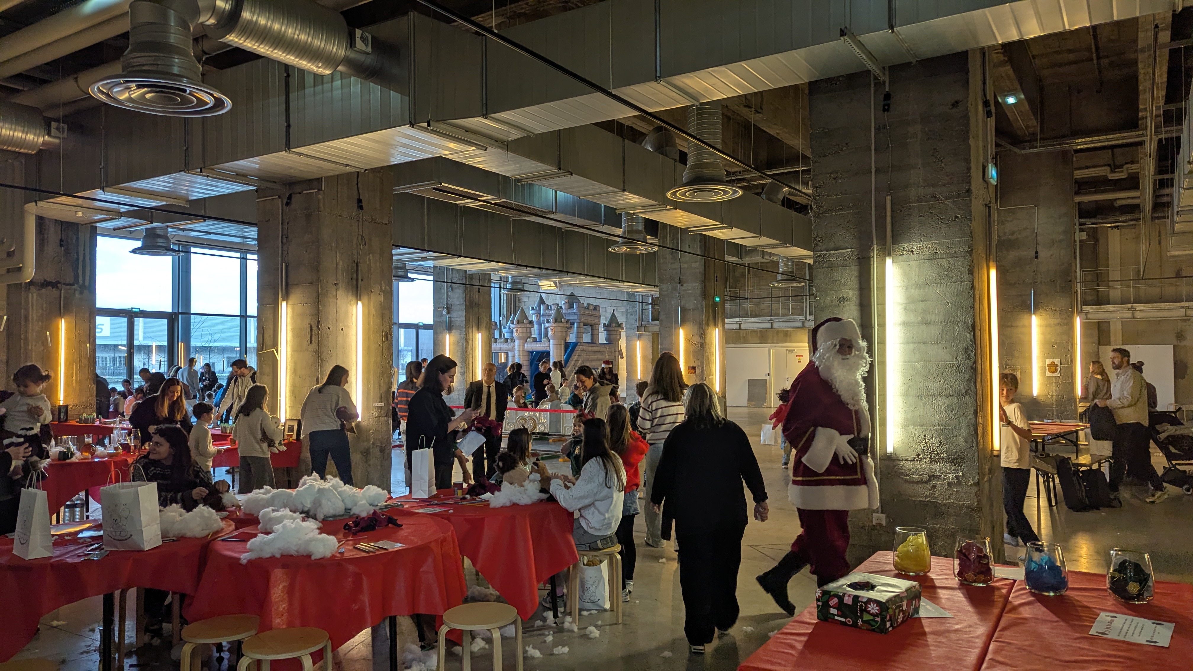 Événement de Noël en intérieur avec tables d’activités pour enfants et personne déguisée en Père Noël dans un grand espace industriel.