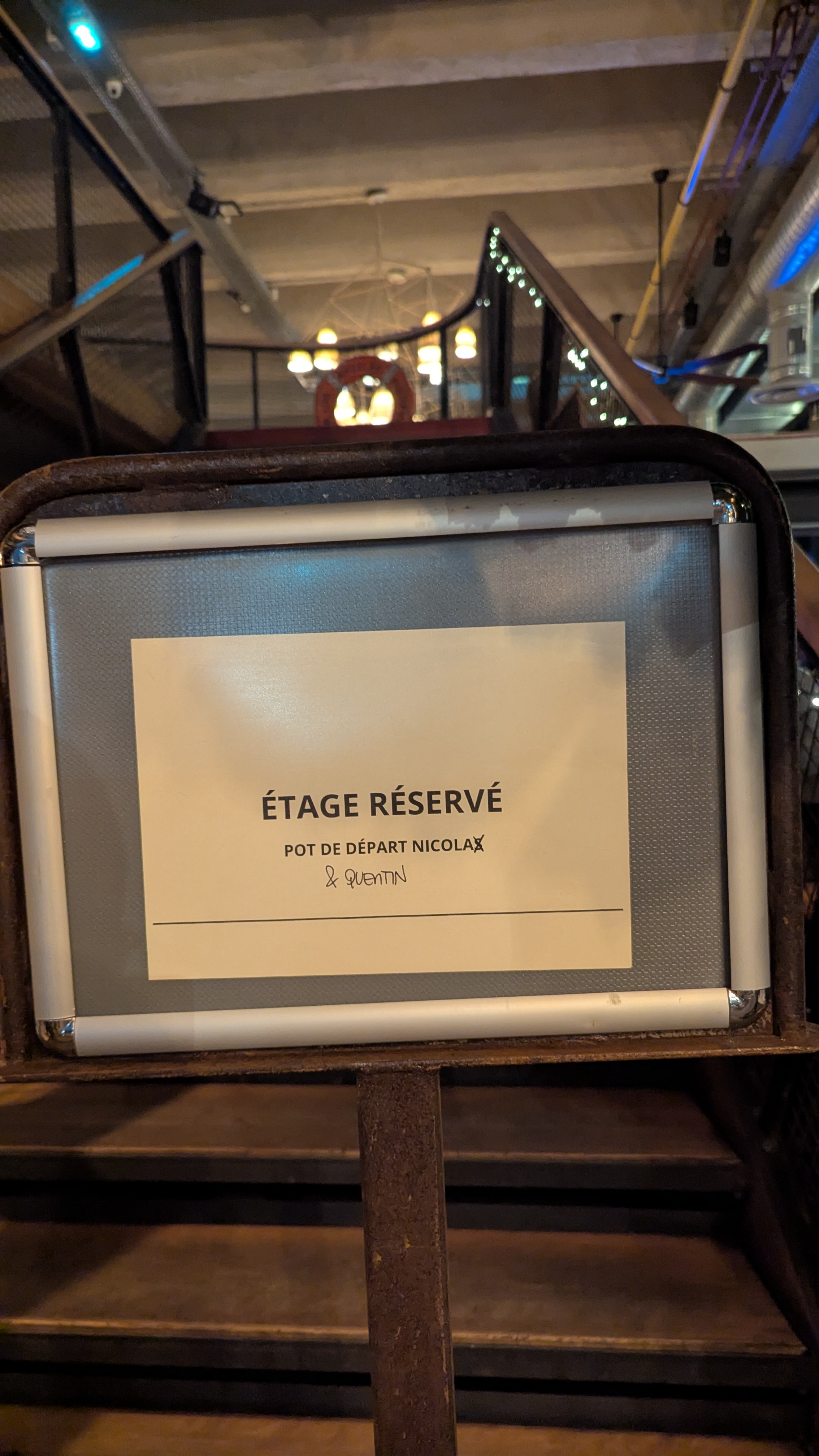 Panneau “Étage réservé – Pot de départ Nicola & Quentin” posé sur un support à l’entrée d’un escalier.