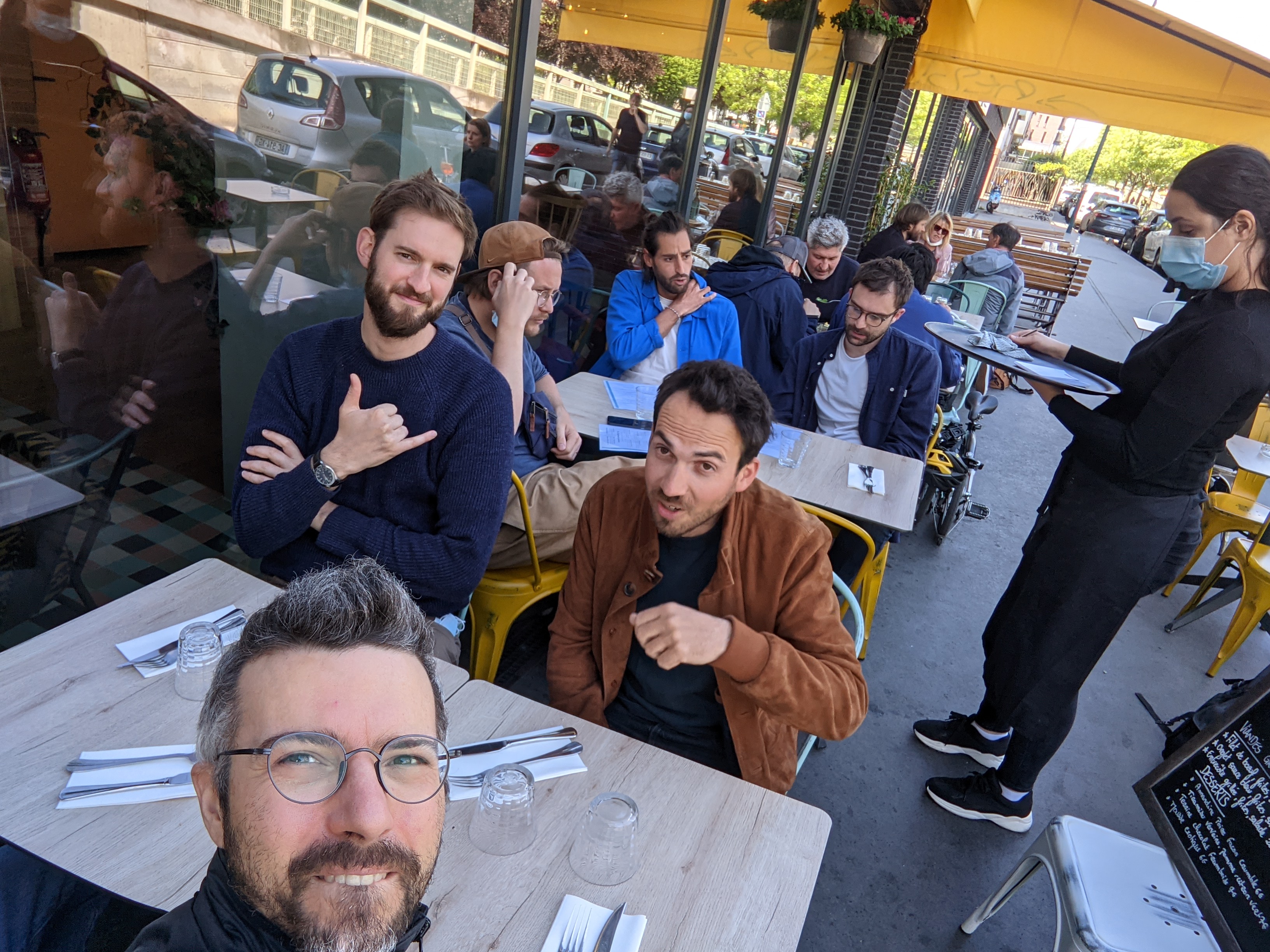 Groupe d’amis attablés en terrasse de café, serveur prenant la commande sur le côté.