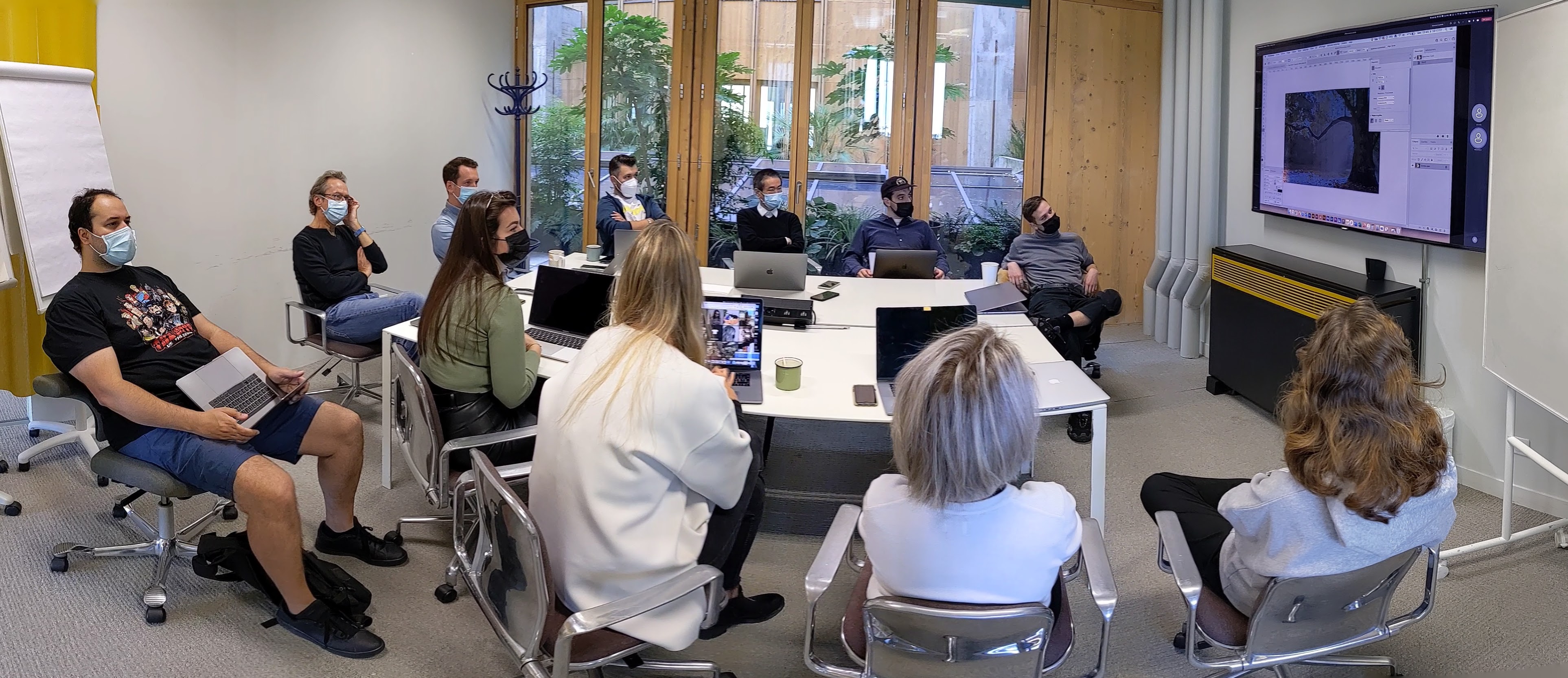 Réunion d’équipe autour d’une table face à un écran affichant une image en cours d’édition.