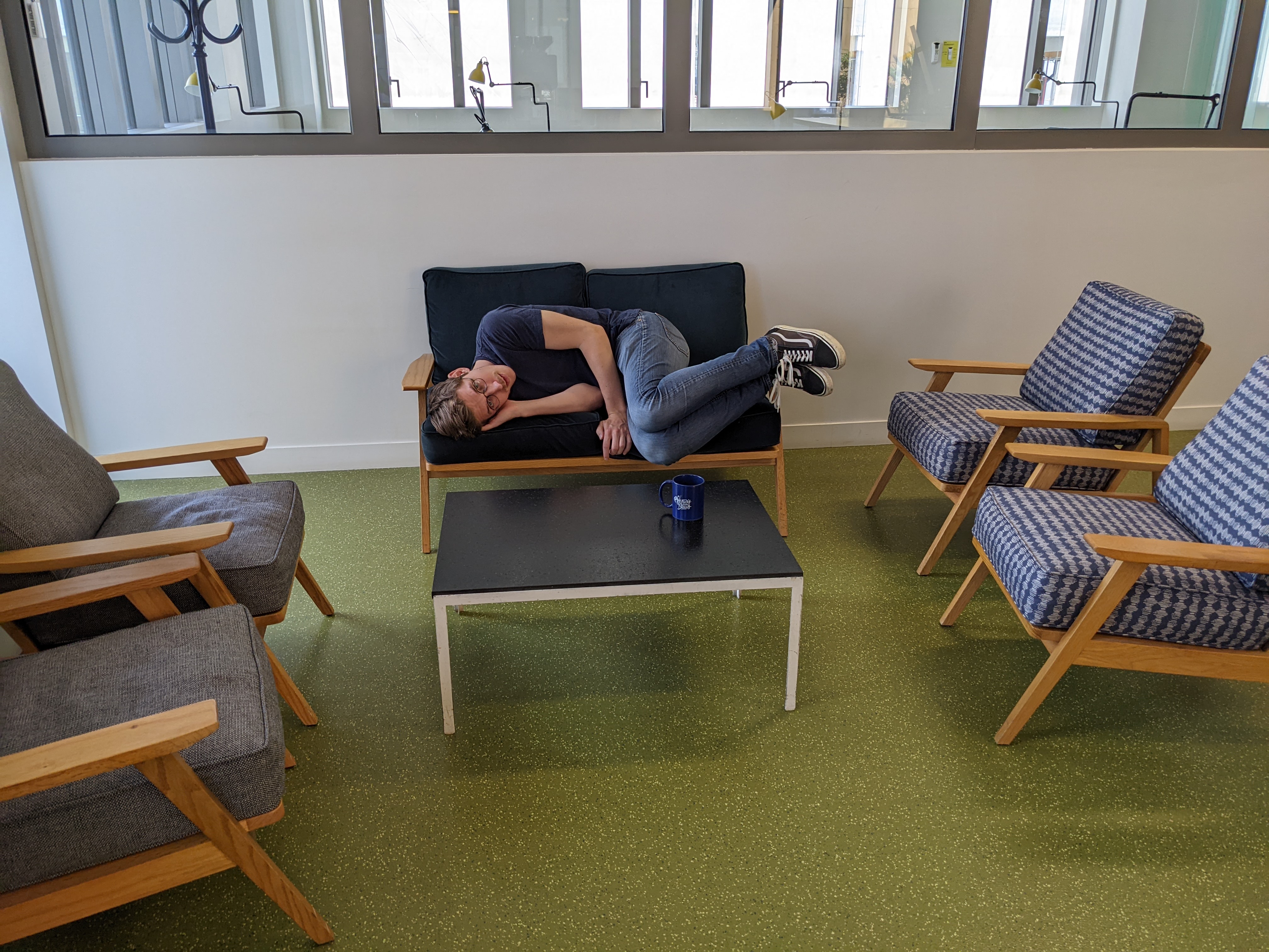 Homme recroquevillé sur un petit canapé dans un espace détente de bureau.