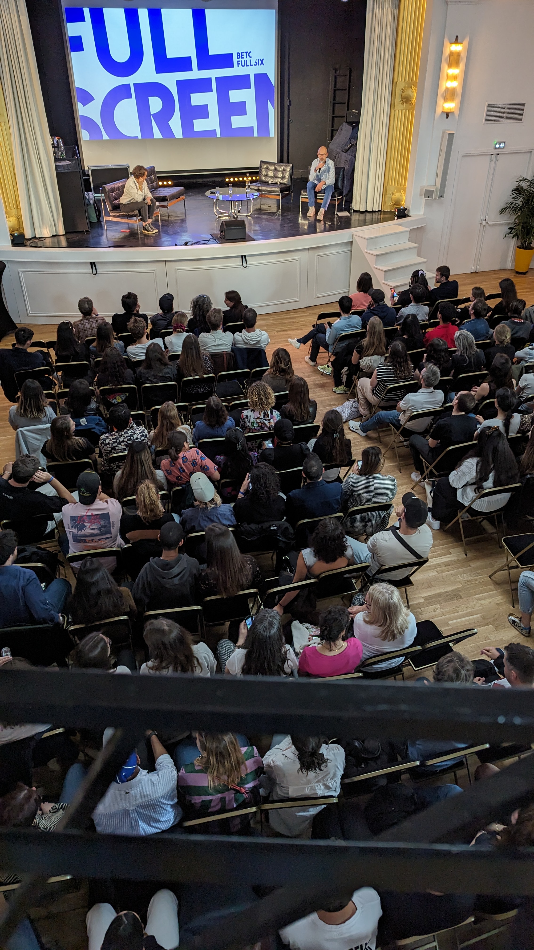 Conférence Full Screen sur scène avec deux intervenants et un public assis dans une salle.