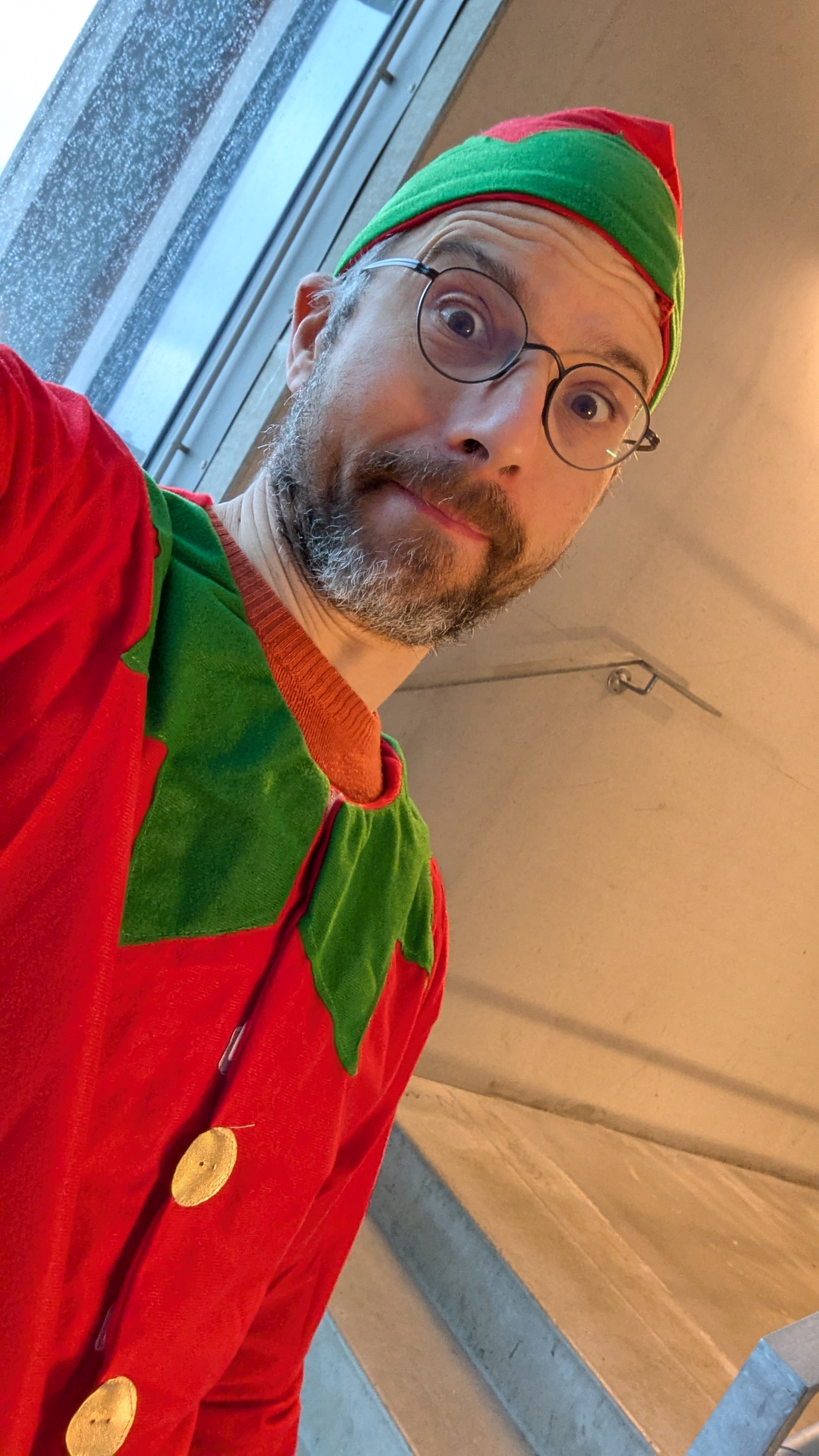 Portrait en gros plan d’un homme déguisé en lutin de Noël, regard amusé vers l’objectif.